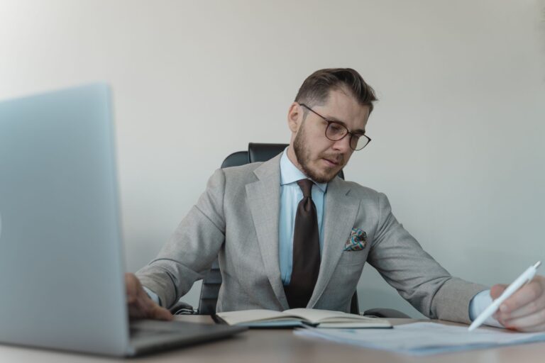 Professional businessman in gray suit working with documents and laptop in modern office.