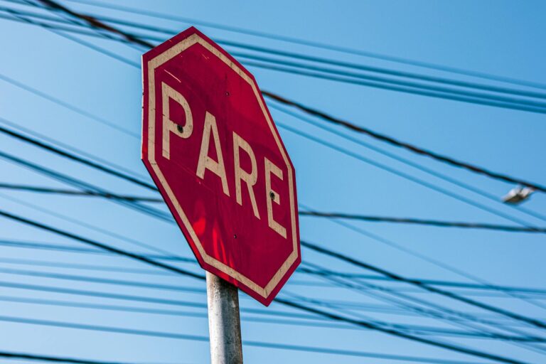 Red stop sign with 'PARE' text against a clear blue sky and overhead power lines.