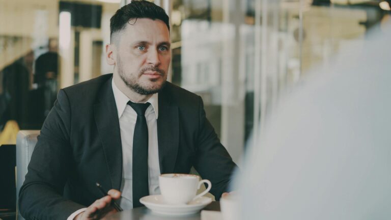 A professional in a suit engaged in a meeting over coffee in a modern café setting.
