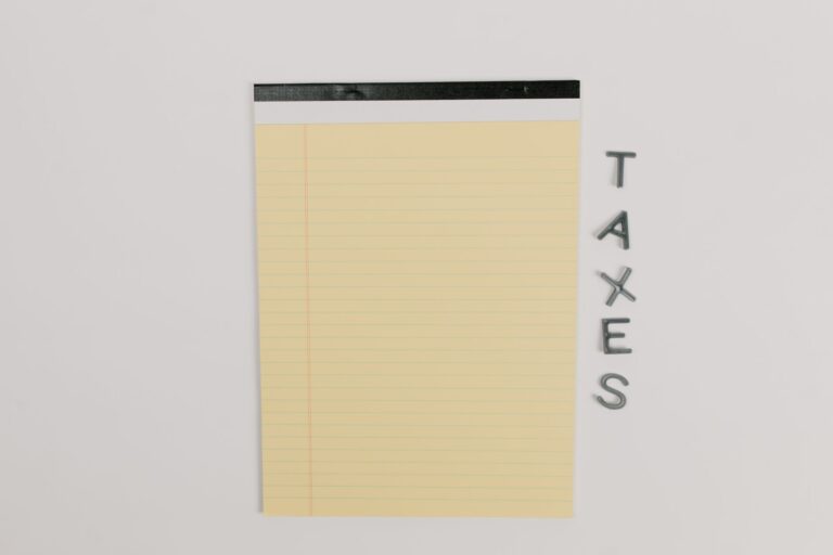 Close-up of a yellow legal pad and the word 'TAXES' on a white surface, ideal for finance themes.