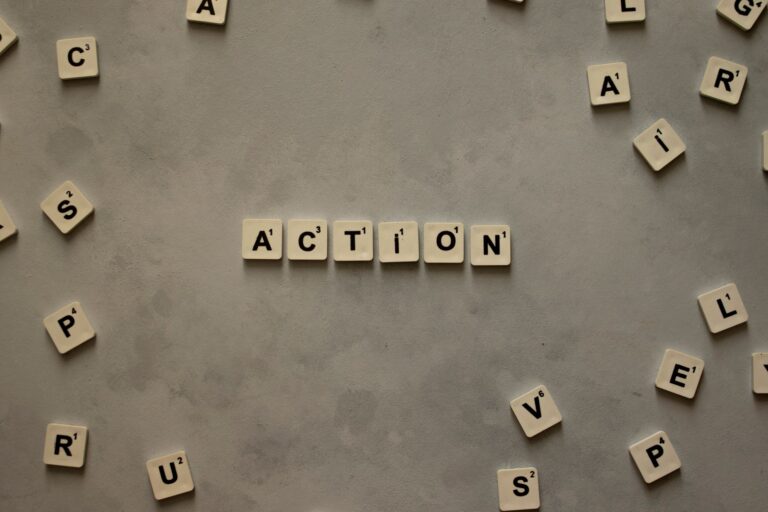 Flat lay of Scrabble tiles spelling 'Action' on a gray background, surrounded by random letters.