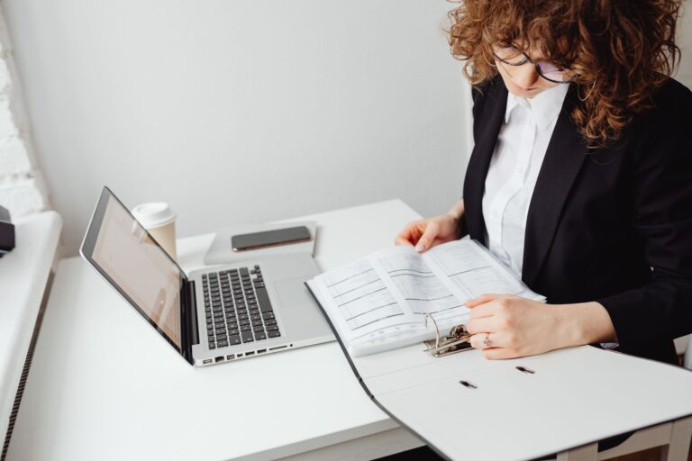Businesswoman reading documents on a laptop in a home office setting. Ideal for work-from-home themes.